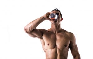 Muscular shirtless male bodybuilder drinking protein shake from blender