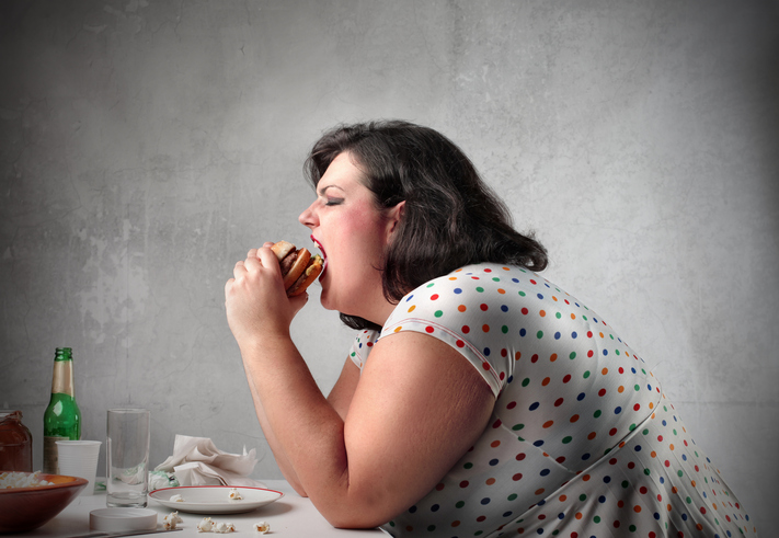 An obese woman eating a hamburger and being gluttonous