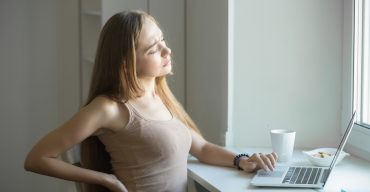 Profile portrait of a young woman, stretching working at laptop