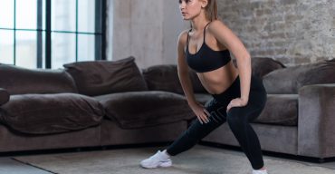 Attractive young woman training indoors doing side lunges working out legs, hips and buttocks