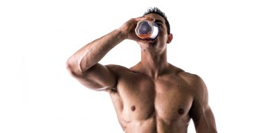 Muscular shirtless male bodybuilder drinking protein shake from blender