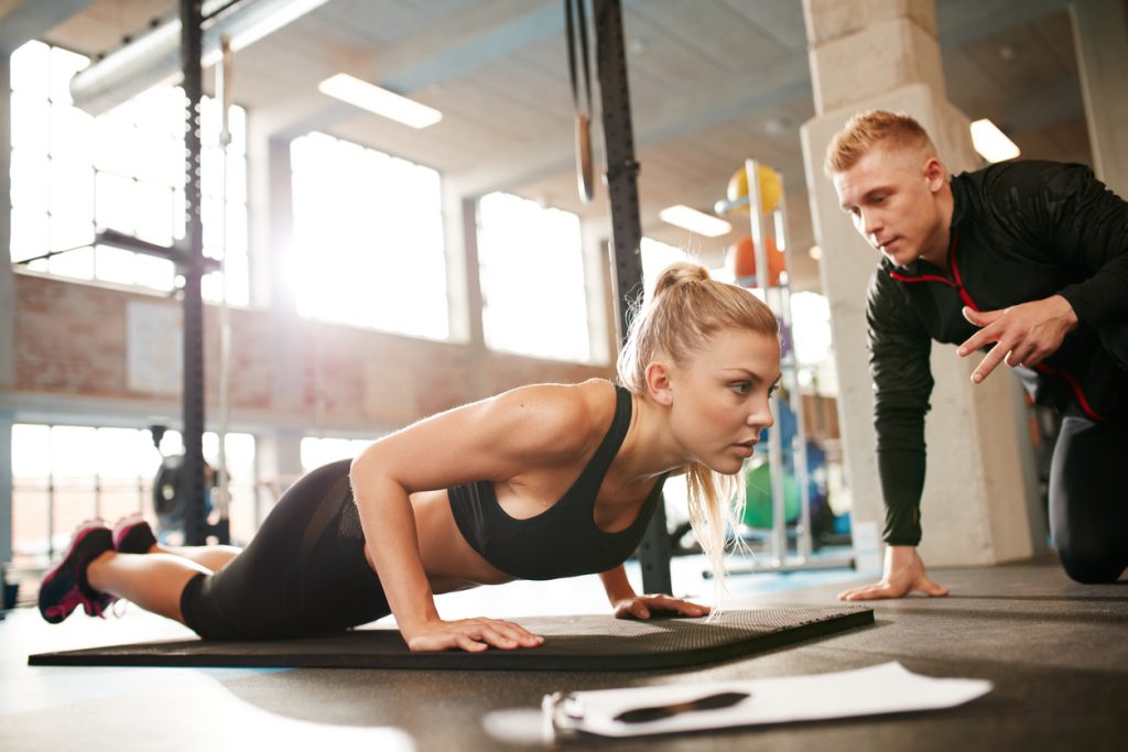 Female exercising with personal trainer at gym