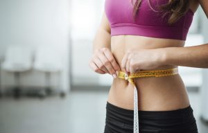 Slim young woman measuring her thin waist with a tape measure, close up