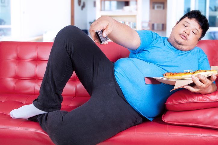 Obese man holds pizza and remote