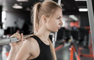 Young blonde woman doing exercises with barbell in gym