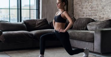 Pretty fit woman doing frontal lunges or squat exercise indoors in a flat