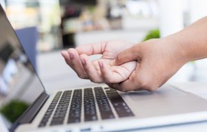 Woman holding and pressing or touching her hand while working with laptop in the office. Numbness or pain on hand concept.